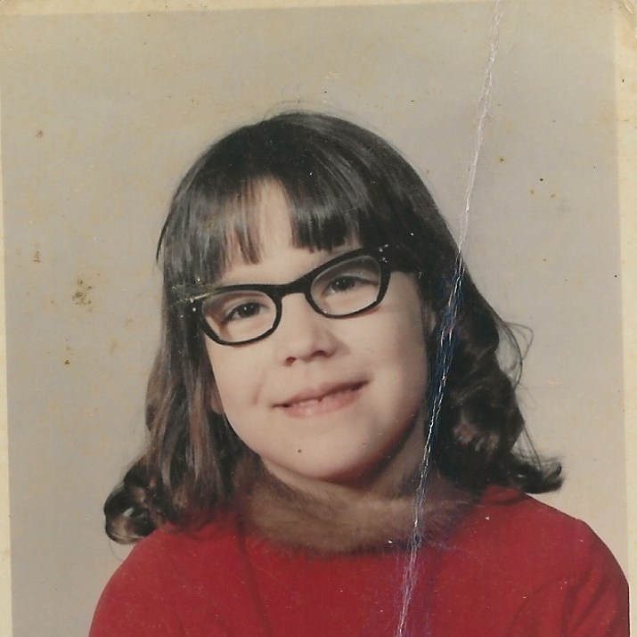 First grade school picture of little girl with brown bangs and glasses